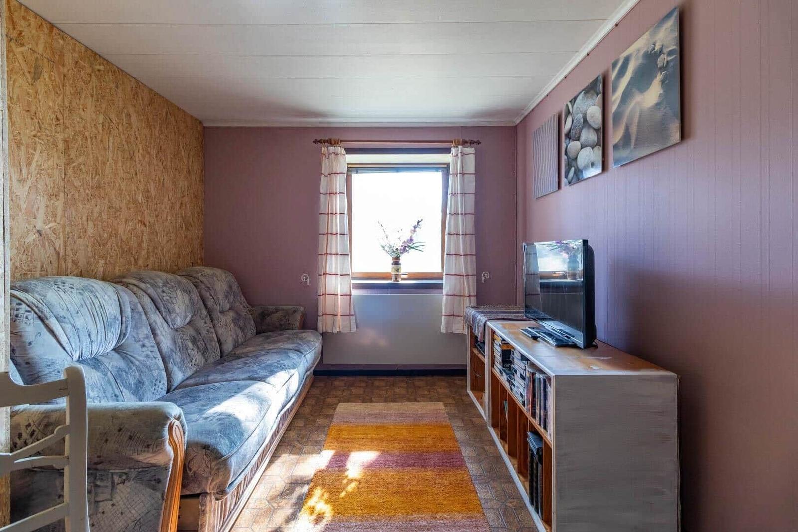 Wohnzimmer mit Sofa, Fernseher und Fenster mit Vorhängen.