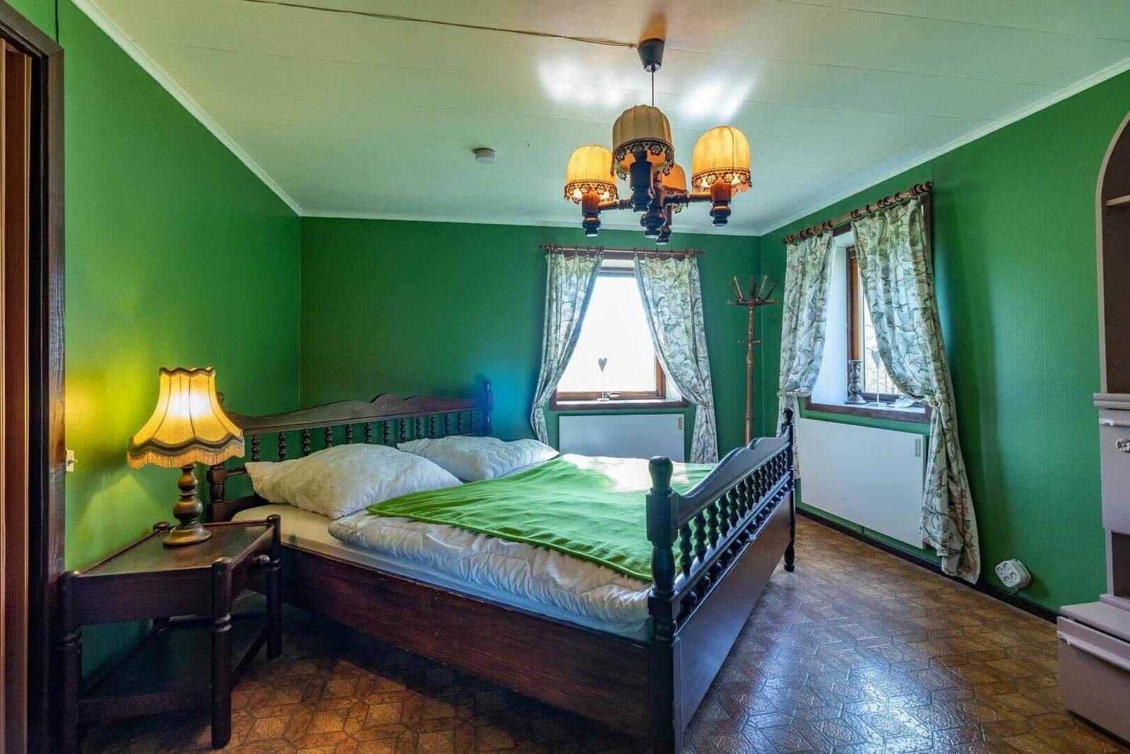 Schlafzimmer mit grünen Wänden, Holzbett und Kronleuchter.