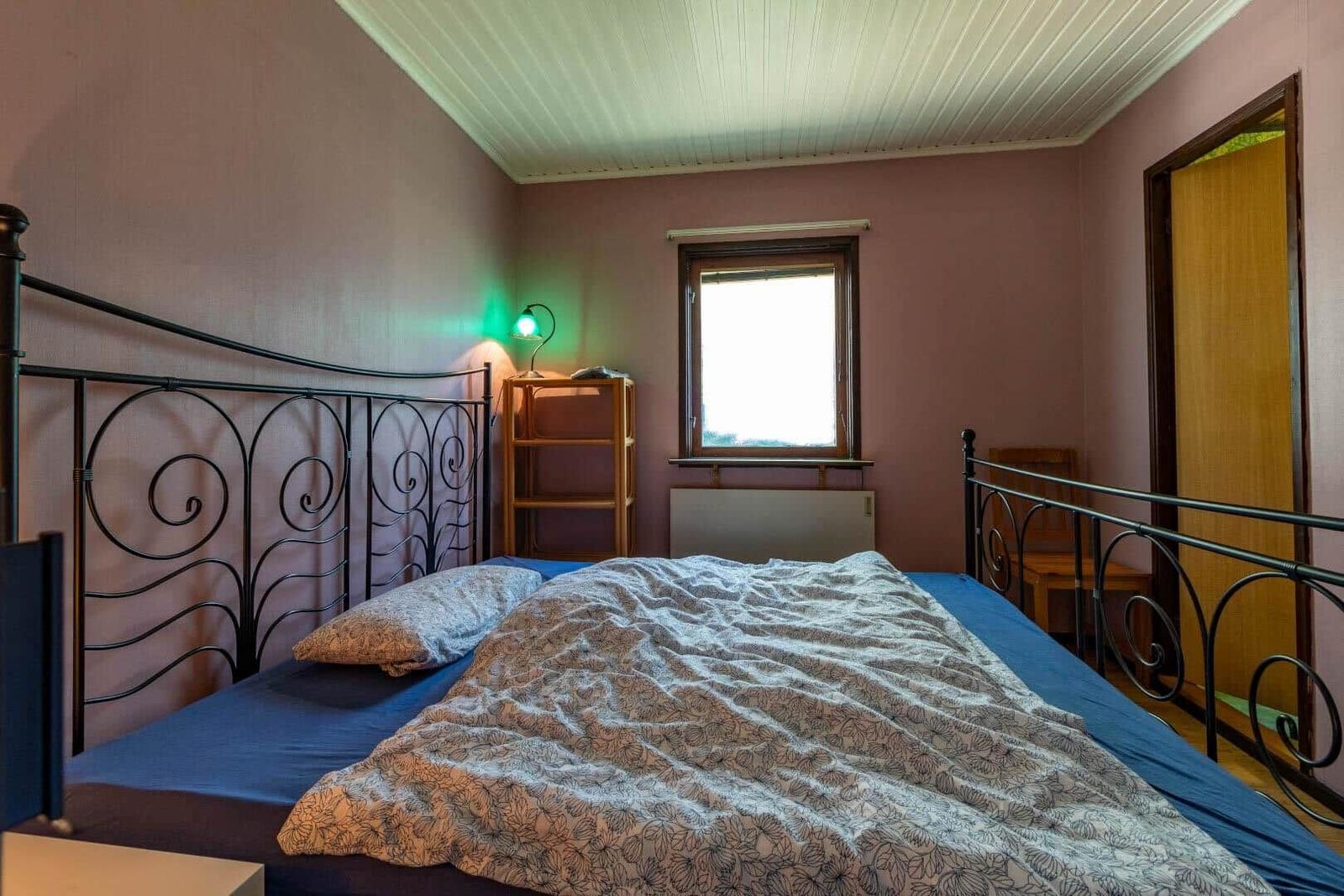 Schlafzimmer mit Metallbett, Fenster und Nachttisch mit Lampe.