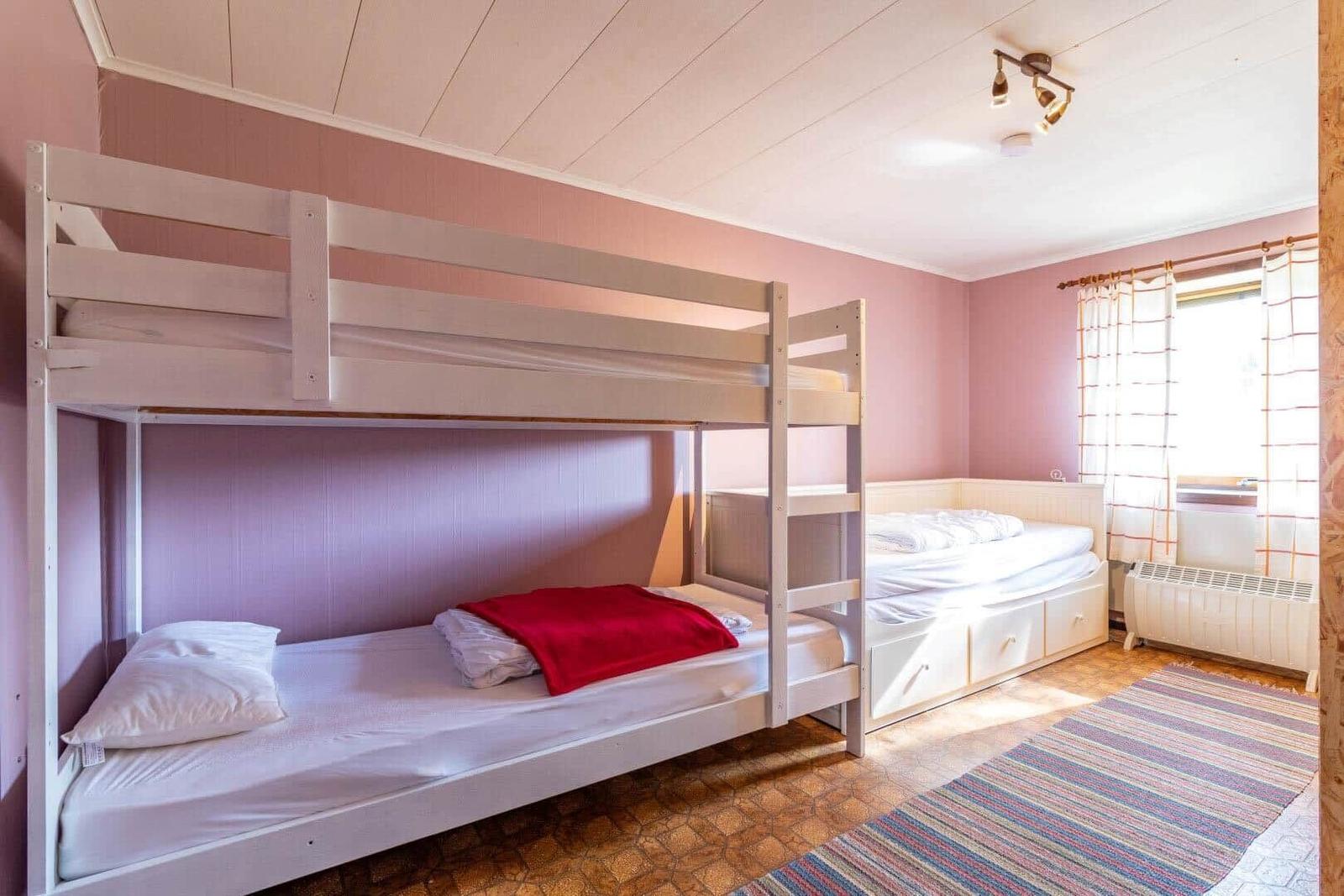 Zimmer mit Doppelstockbett und Einzelbett, rosa Wände und Holzboden.