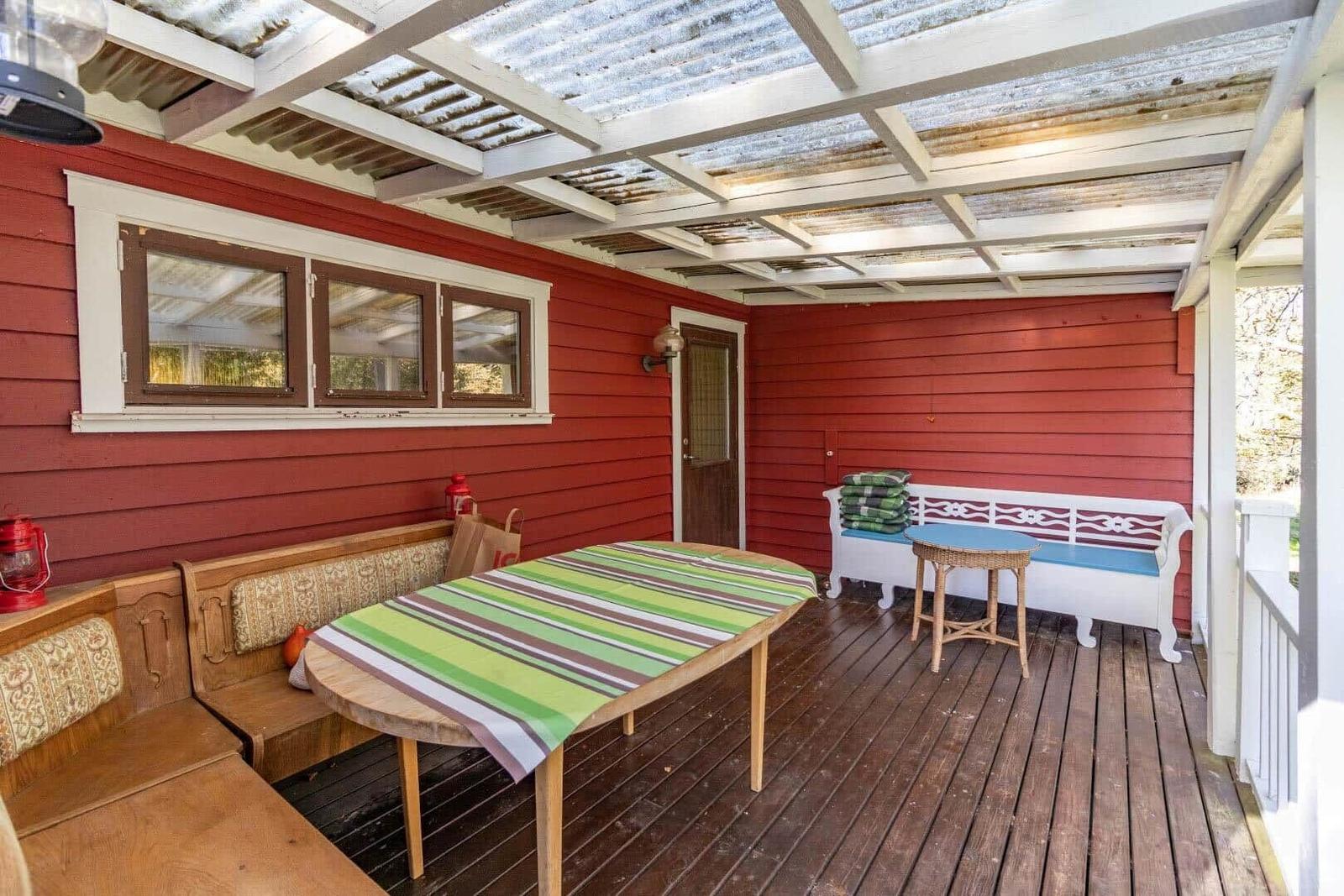 Terrasse mit Holzboden, Tisch, Bänken und roter Wand