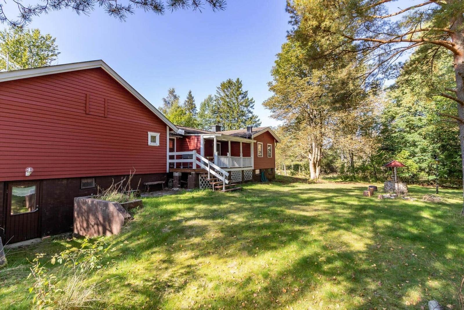 Rotes Holzhaus mit Terrasse und Garten. Umgeben von Bäumen und Gras.