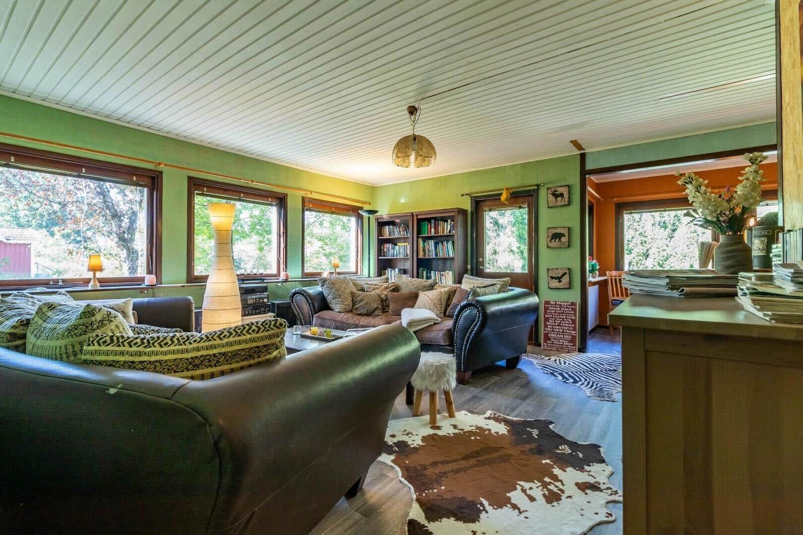 Wohnzimmer mit braunen Ledersofas, Holzboden und großen Fenstern mit Blick auf Bäume.