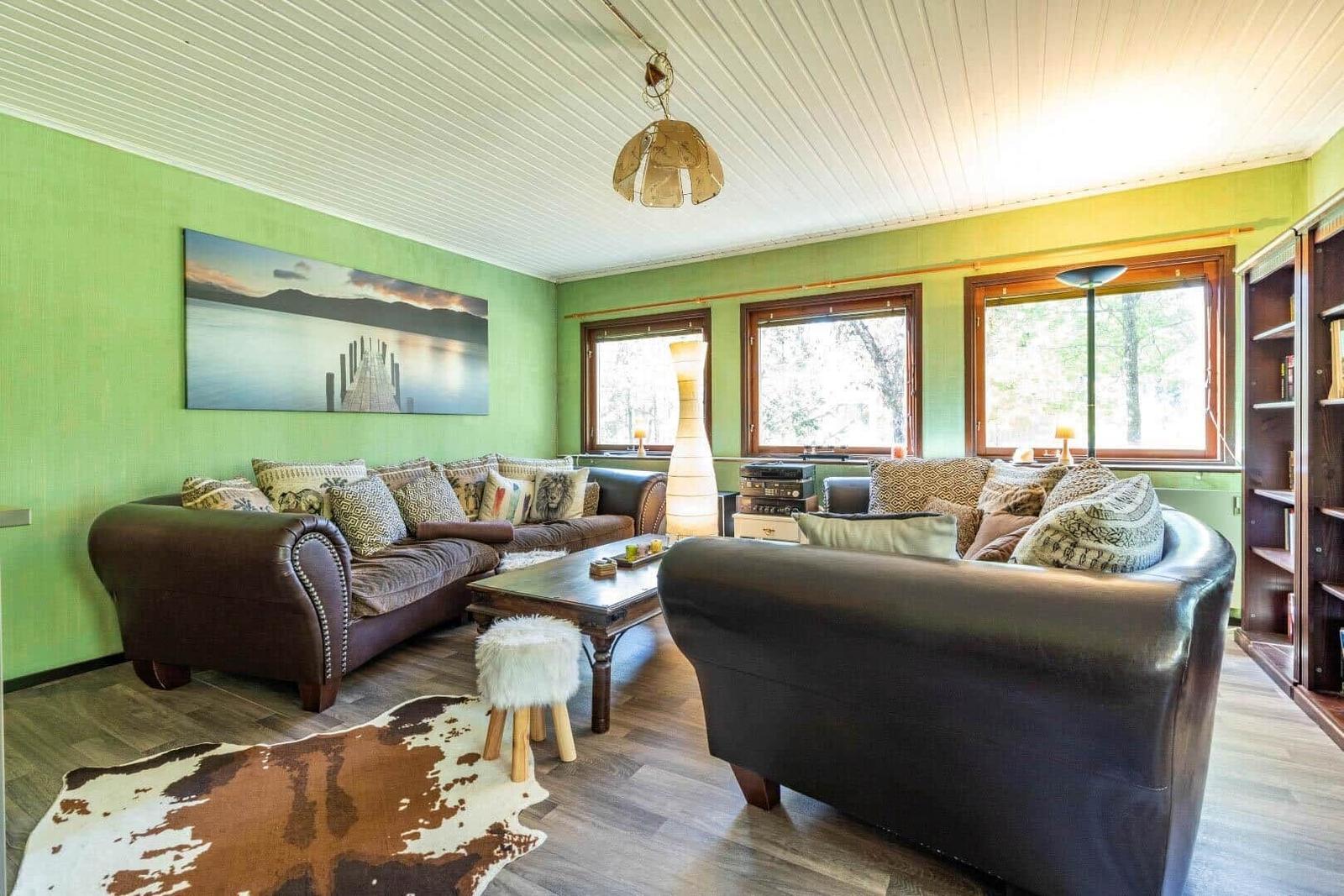 Wohnzimmer mit zwei Ledersofas, Holzboden und grünen Wänden. Fenster und Wandbild sichtbar.