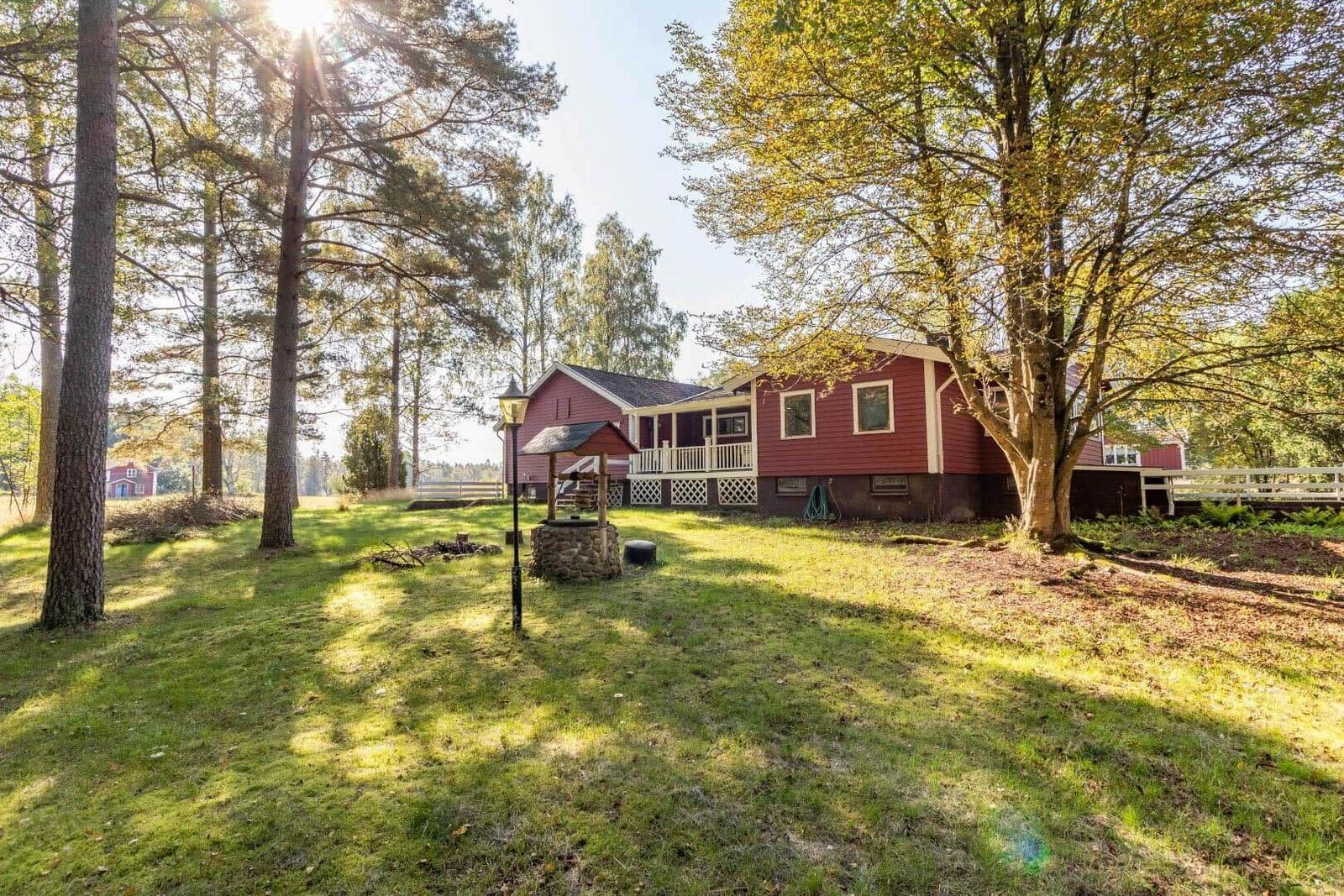 Rotes Haus mit Veranda im Grünen, umgeben von Bäumen und Grasfläche.
