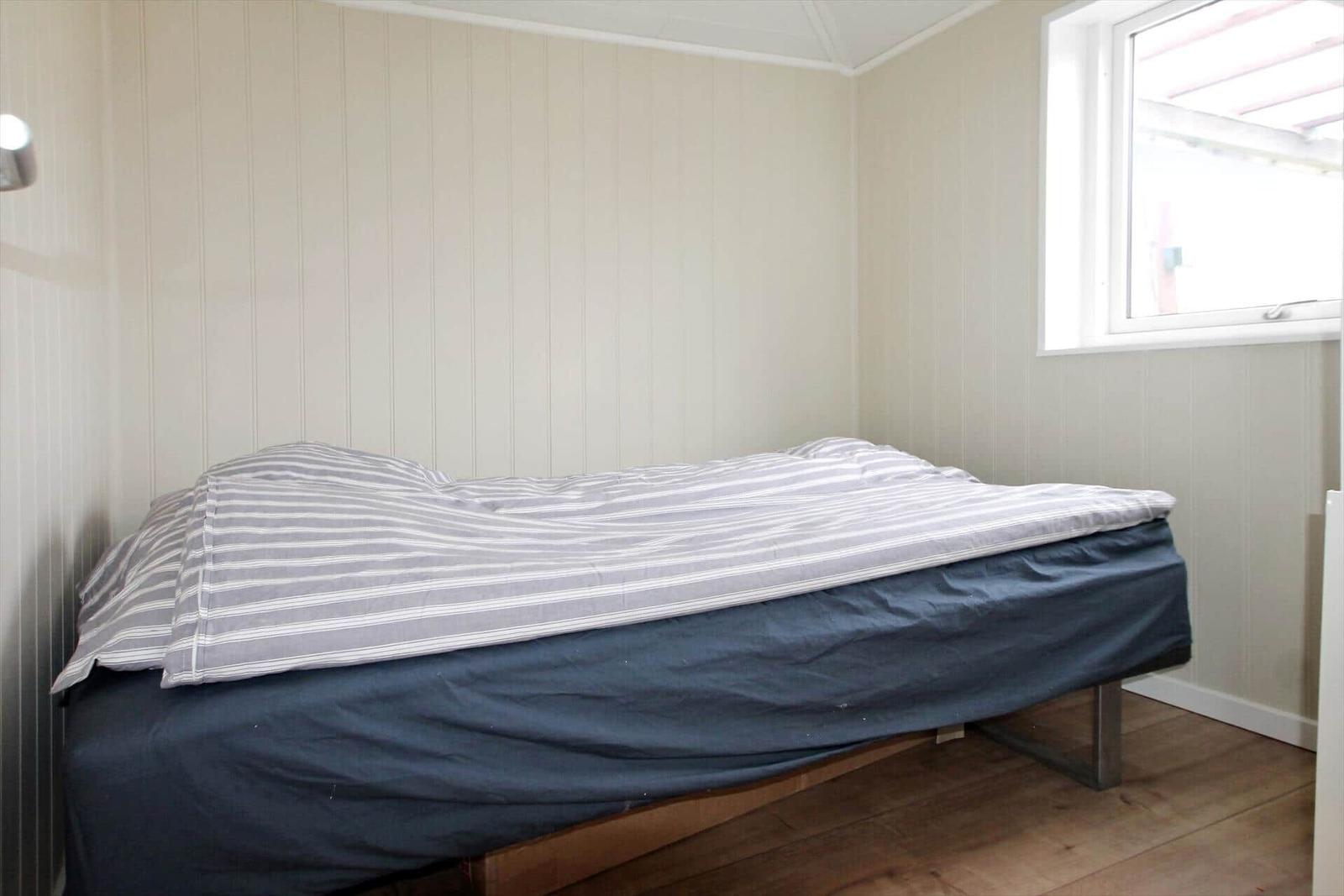 Ein Schlafzimmer mit Bett, Fenster und vertikal verkleideten Wänden.