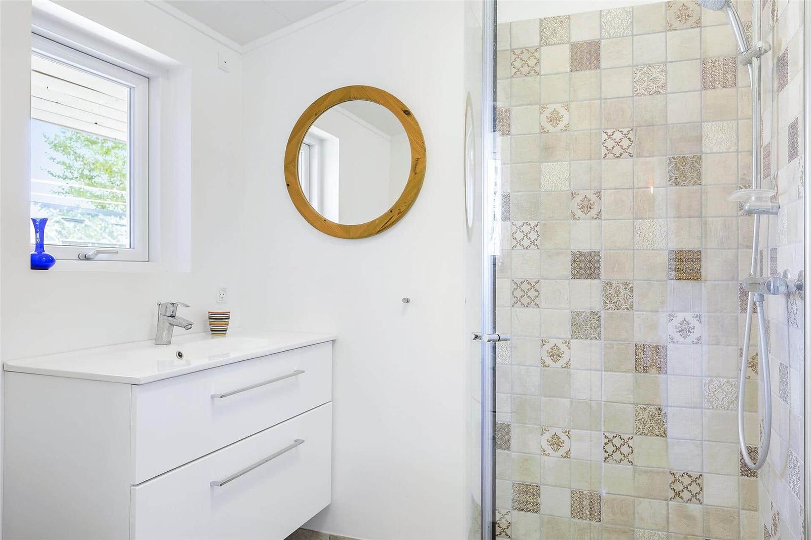 Badezimmer mit Dusche, Waschbecken und runden Spiegel