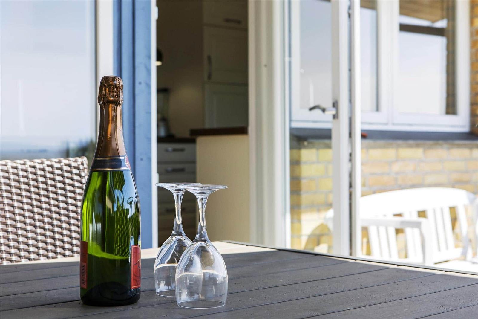 Eine Flasche Sekt und zwei Gläser stehen auf einer Terrastisch. Im Hintergrund ist eine Küche und ein Balkon sichtbar.