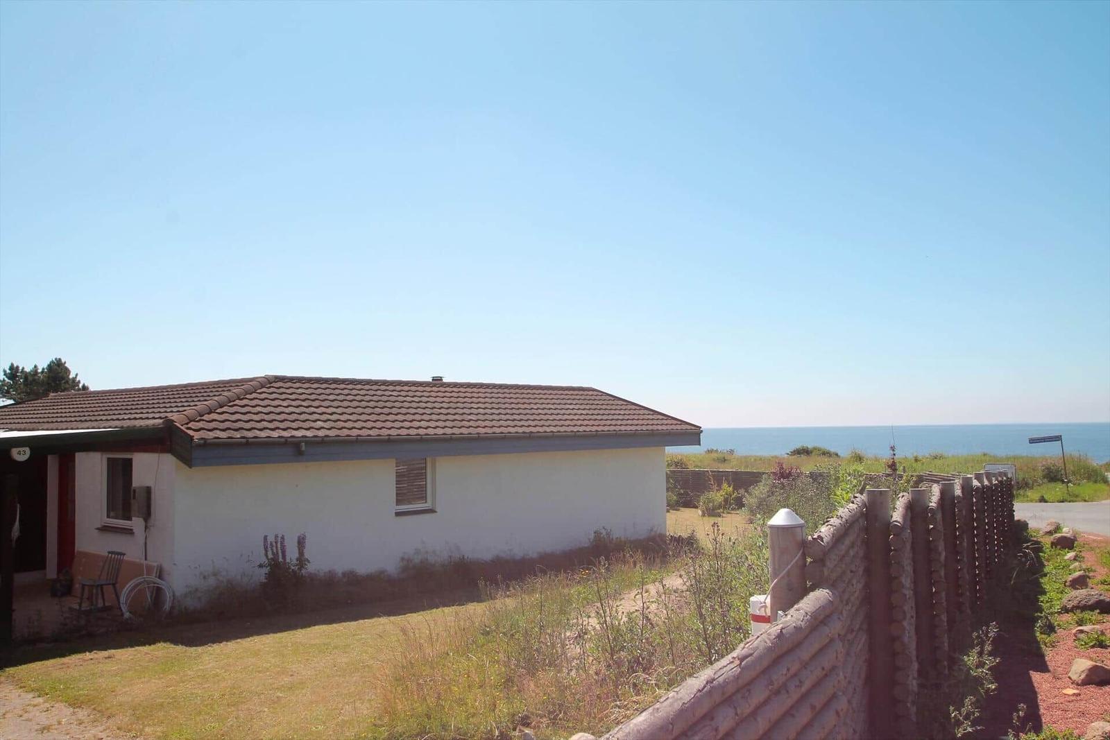 Ein weißes Haus mit braunem Dach, umgeben von Gras und einem Holzzaun, mit Blick auf das Meer.