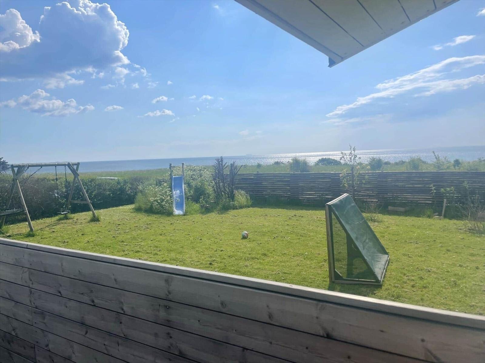 Grüner Garten mit Spielplatz und Meerblick. Holzzaun und blaue Rutsche sind sichtbar.