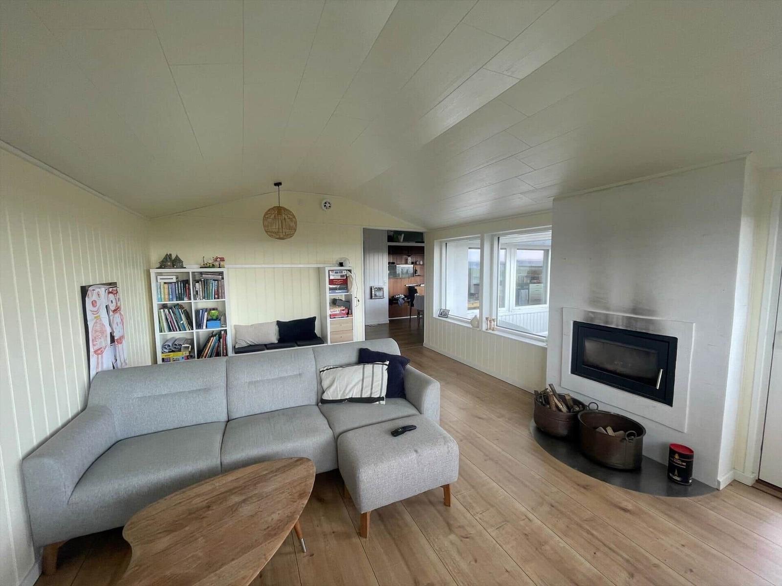 Wohnzimmer mit Sofa, Kamin und Holzboden. Bücherregal und Fenster sichtbar.
