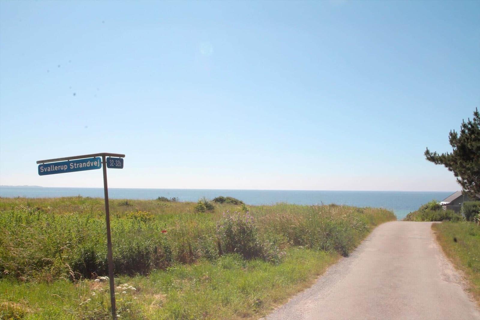 Straßenschild zeigt Svalerup Strandvej. Asphaltweg führt zum Meer mit Grasland und Bäumen.