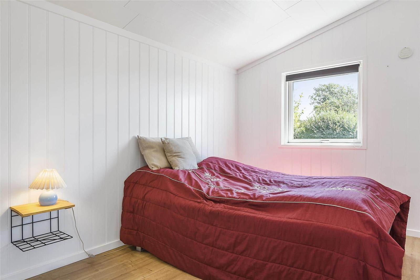 Schlafzimmer mit Bett, Fenster und Nachttisch mit Lampe.