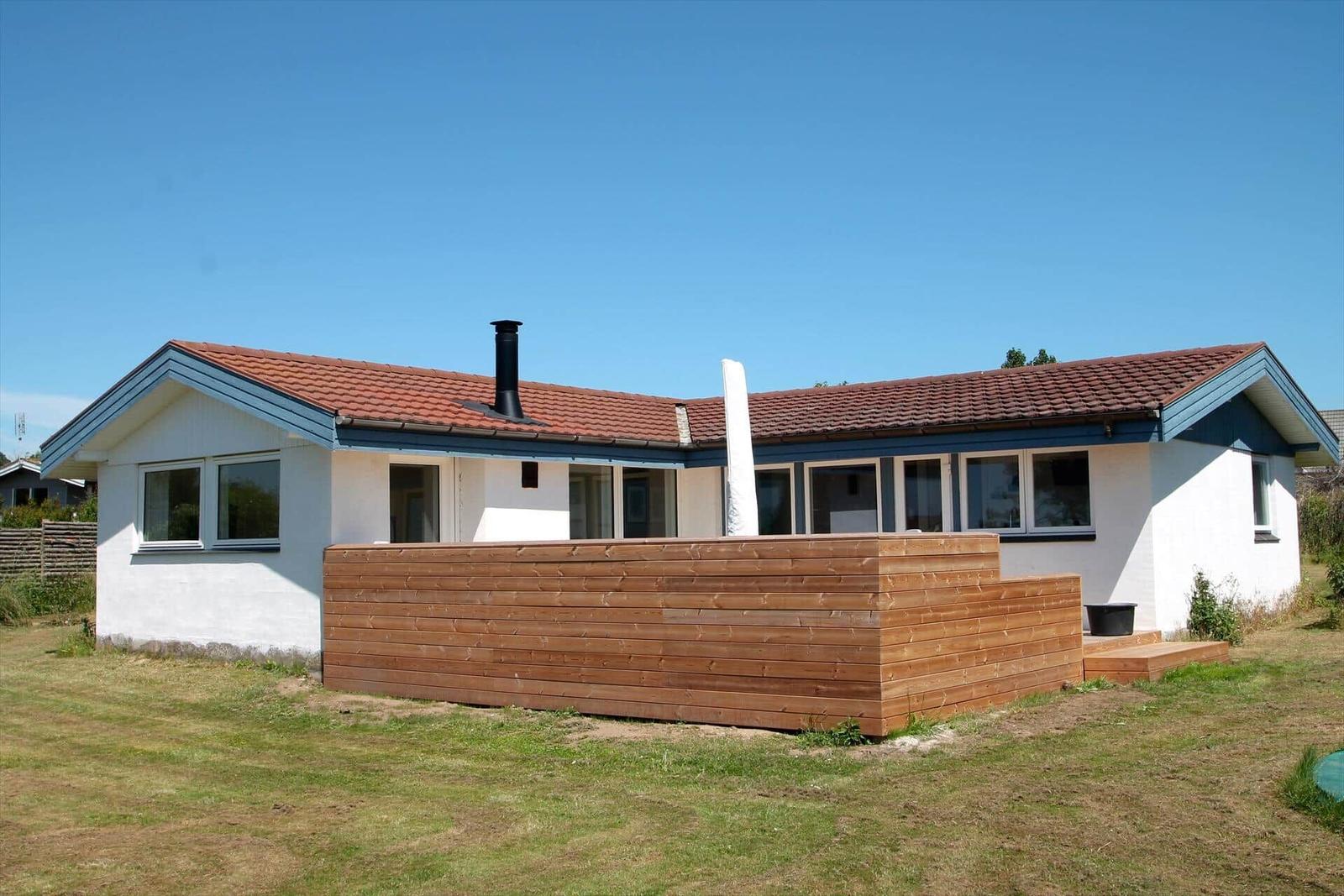 Wohnhaus mit Holzterrasse und rotem Dach unter blauem Himmel.