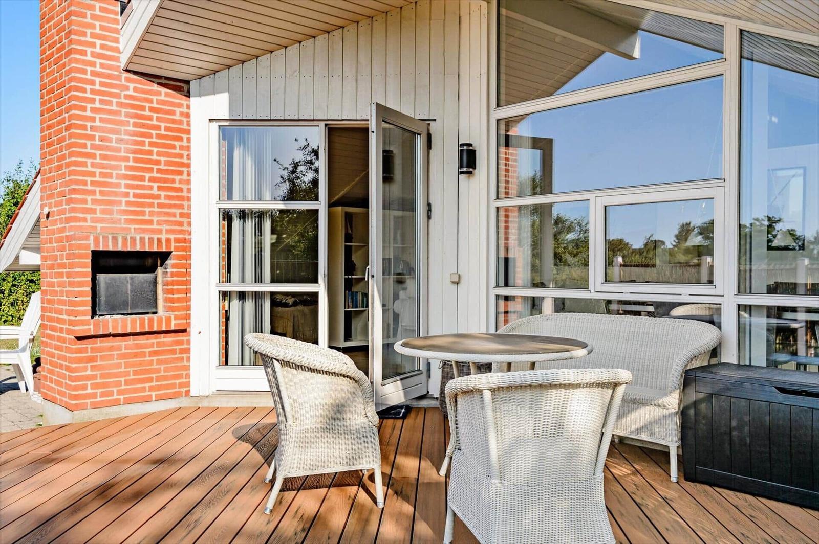 Deck with table and chairs, glass facade and brick wall. Door leads inside.