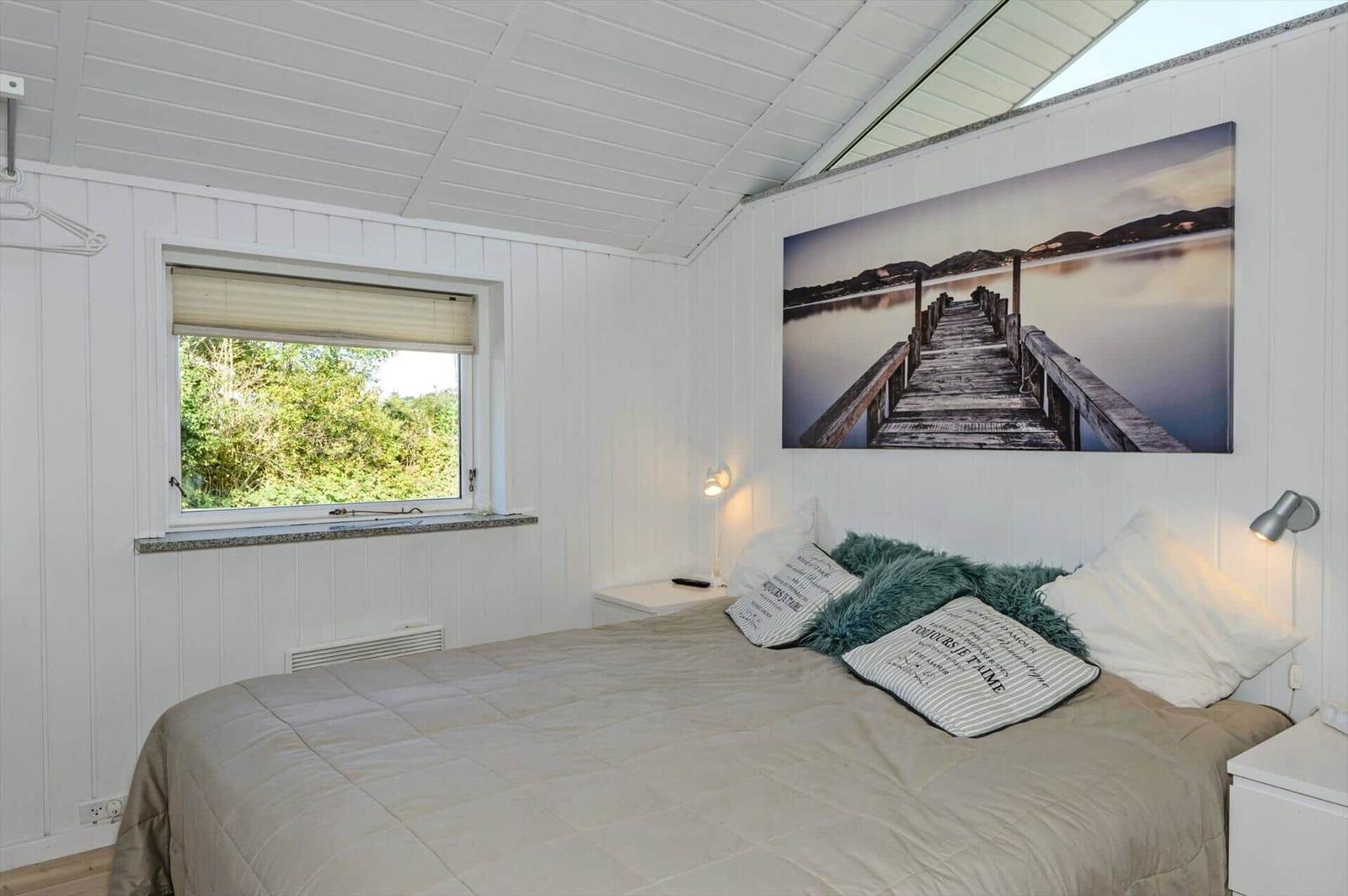 Bedroom with bed, wall art, and window with view of greenery.