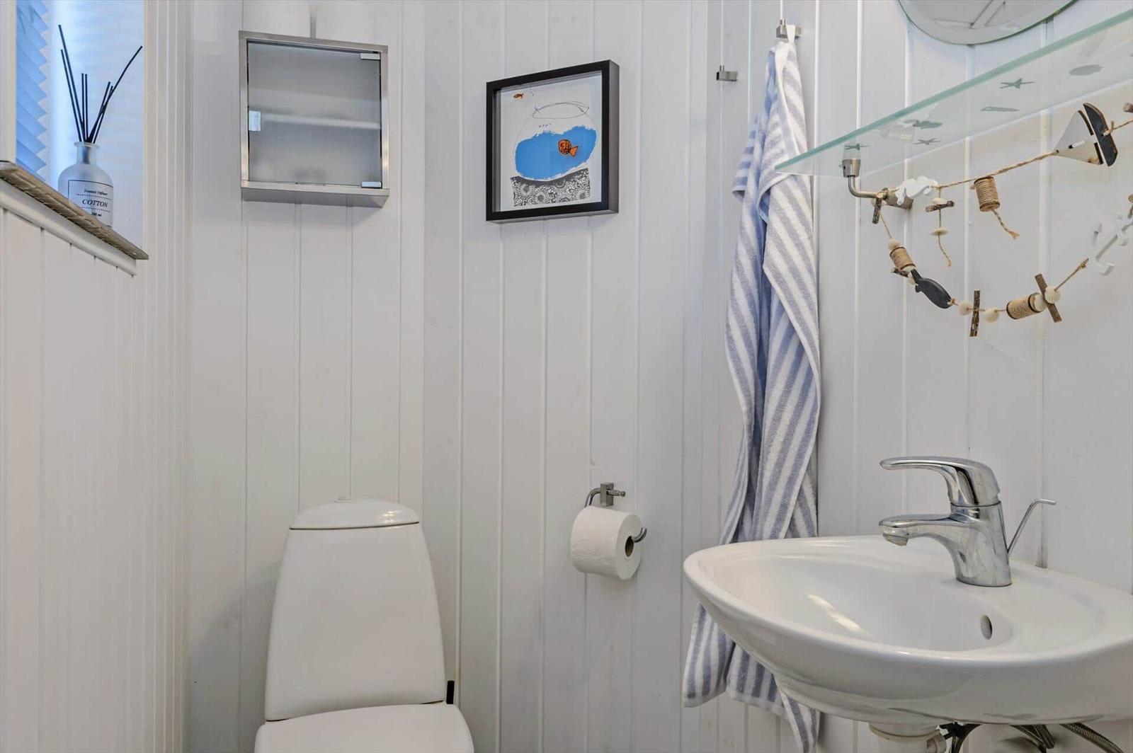 Bathroom with toilet, sink, and mirror. Wall decor with picture and towel.