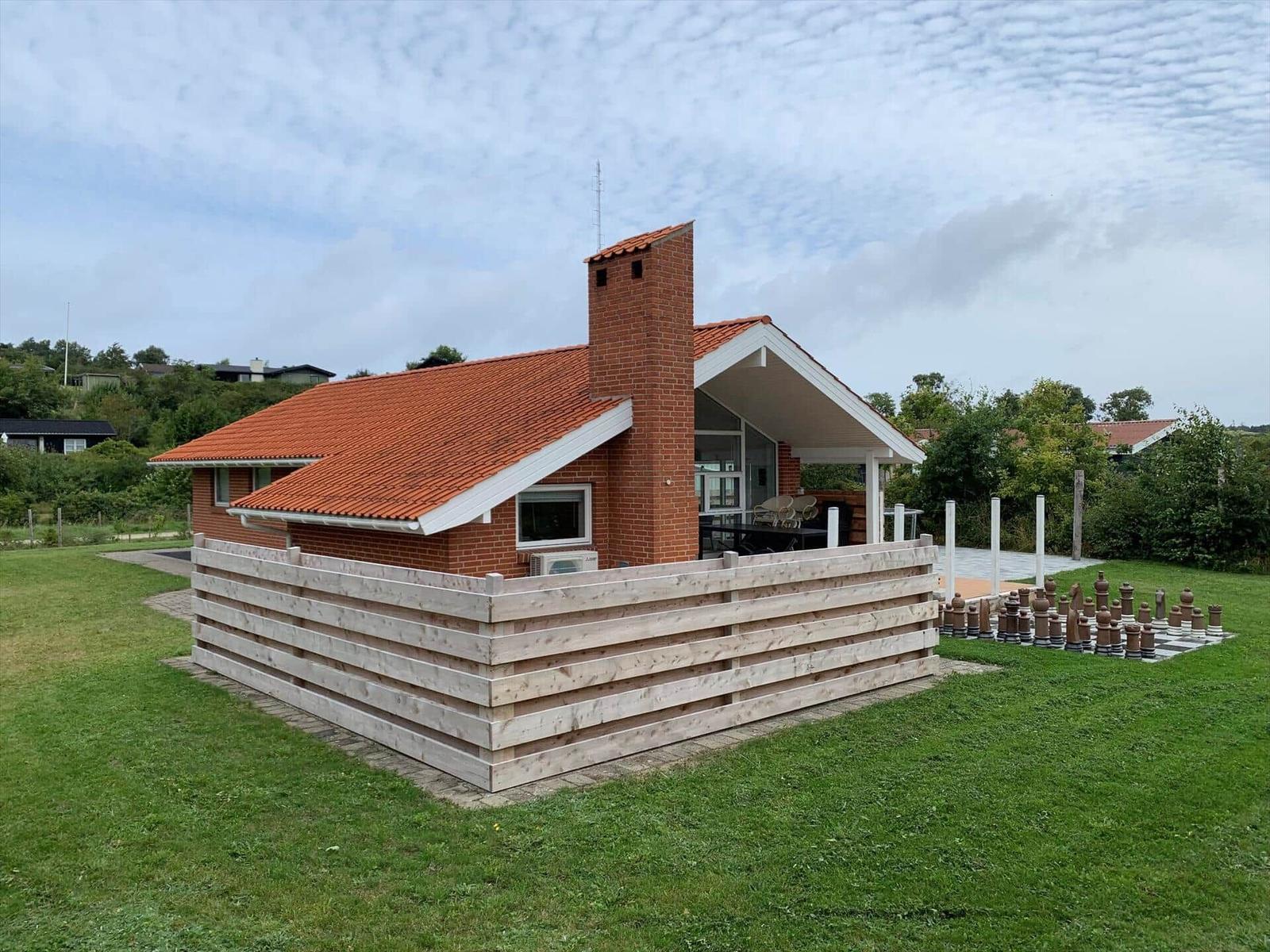 A house with a red roof and wooden fence. A large chessboard is on the property.