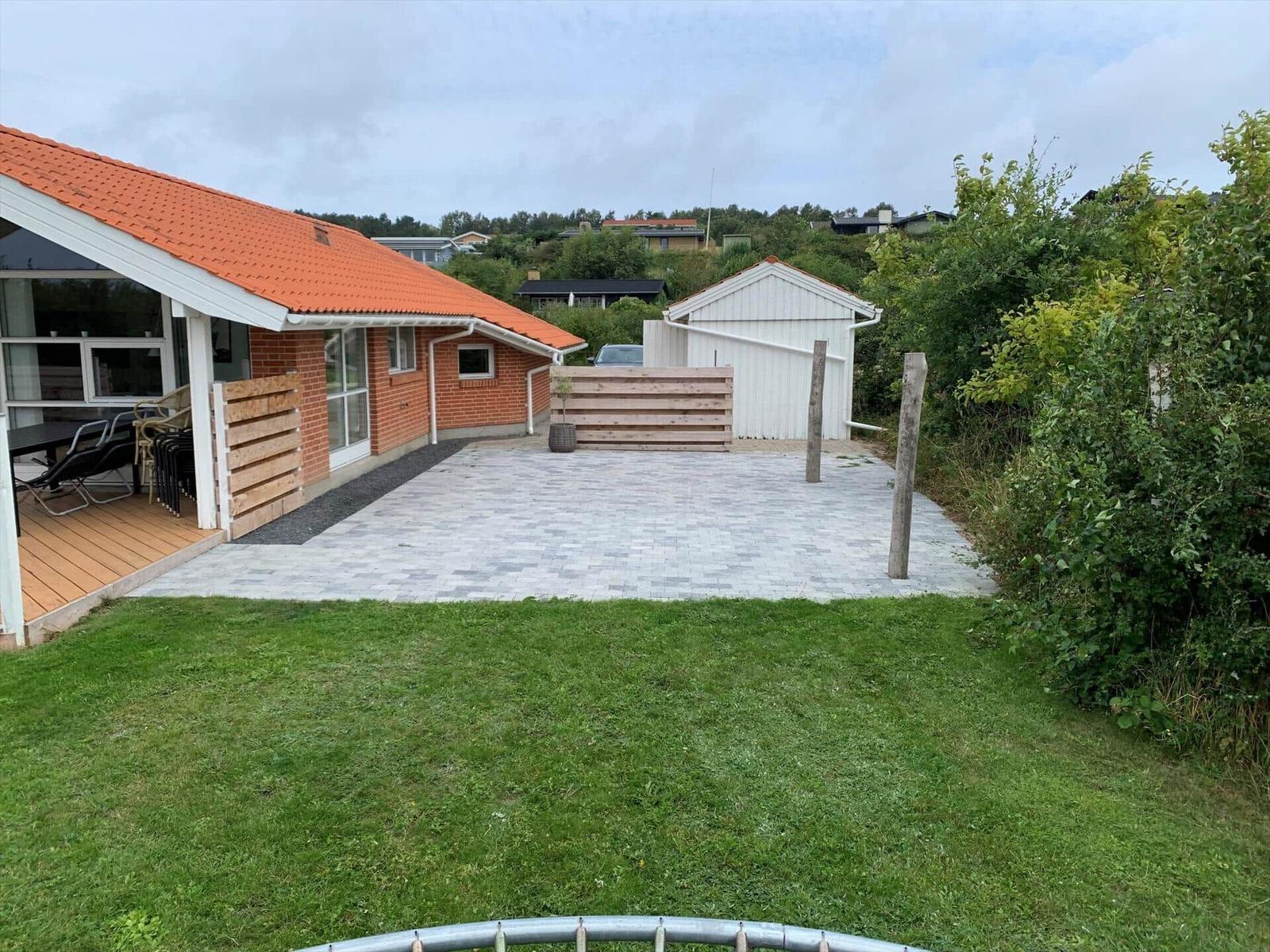 House with terrace, paved yard, and garden. White shed and green trees are visible.