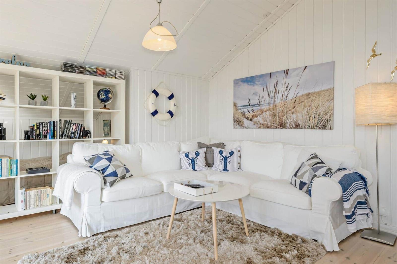 Living room with white sofa, beach artwork, and bookshelf against wall.