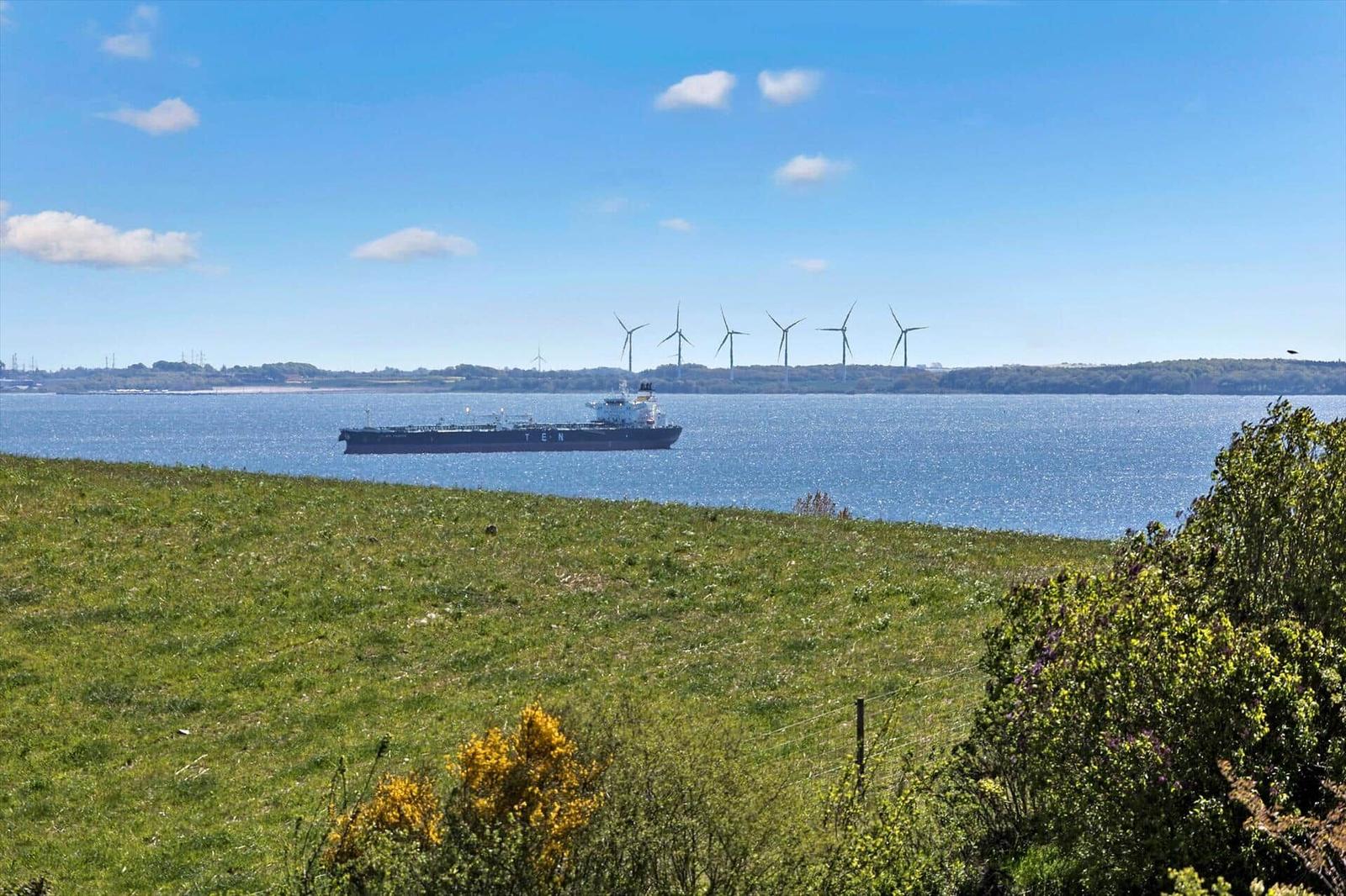 Green field with view of sea, shipyard, and wind turbines in the background.