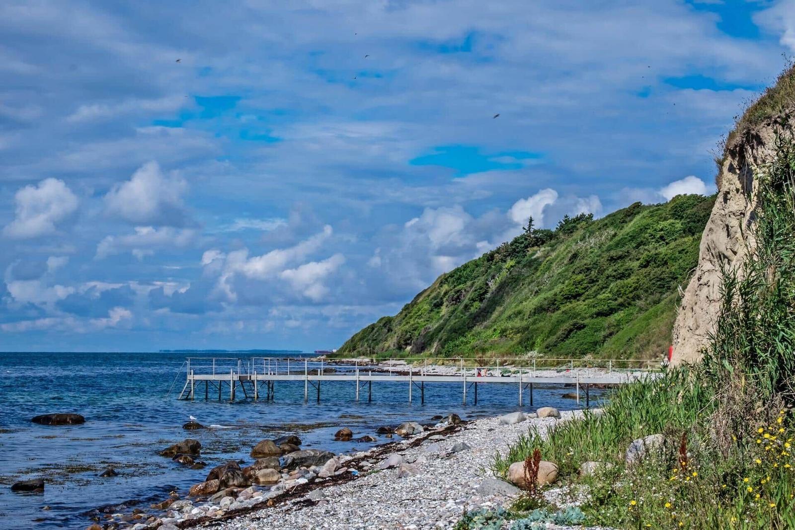 Dock, beach, and green cliff under blue sky.