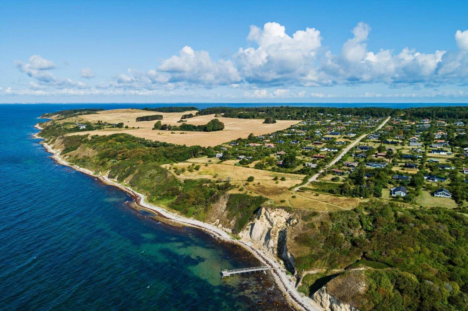Aerial view of coastal village with cliffs, fields, and houses near the sea.