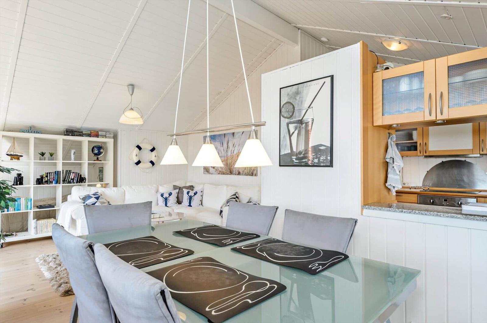 Dining area with glass table and gray chairs. Kitchen with wooden cabinets and white walls.