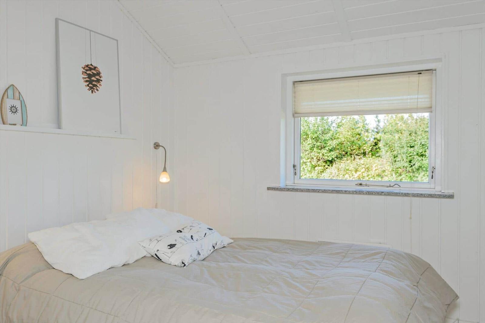 A bedroom with white wood paneling, a bed, and a window with a view of trees.