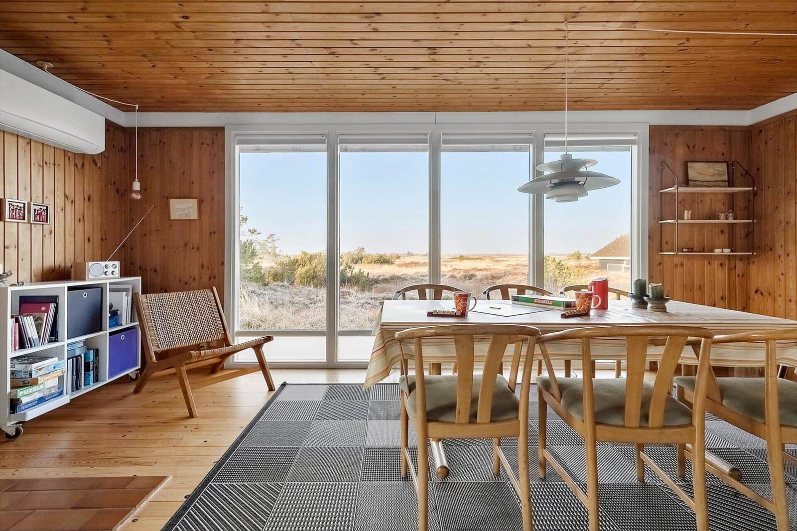 Esszimmer mit Holzwand und großem Fensterblick auf die Landschaft.