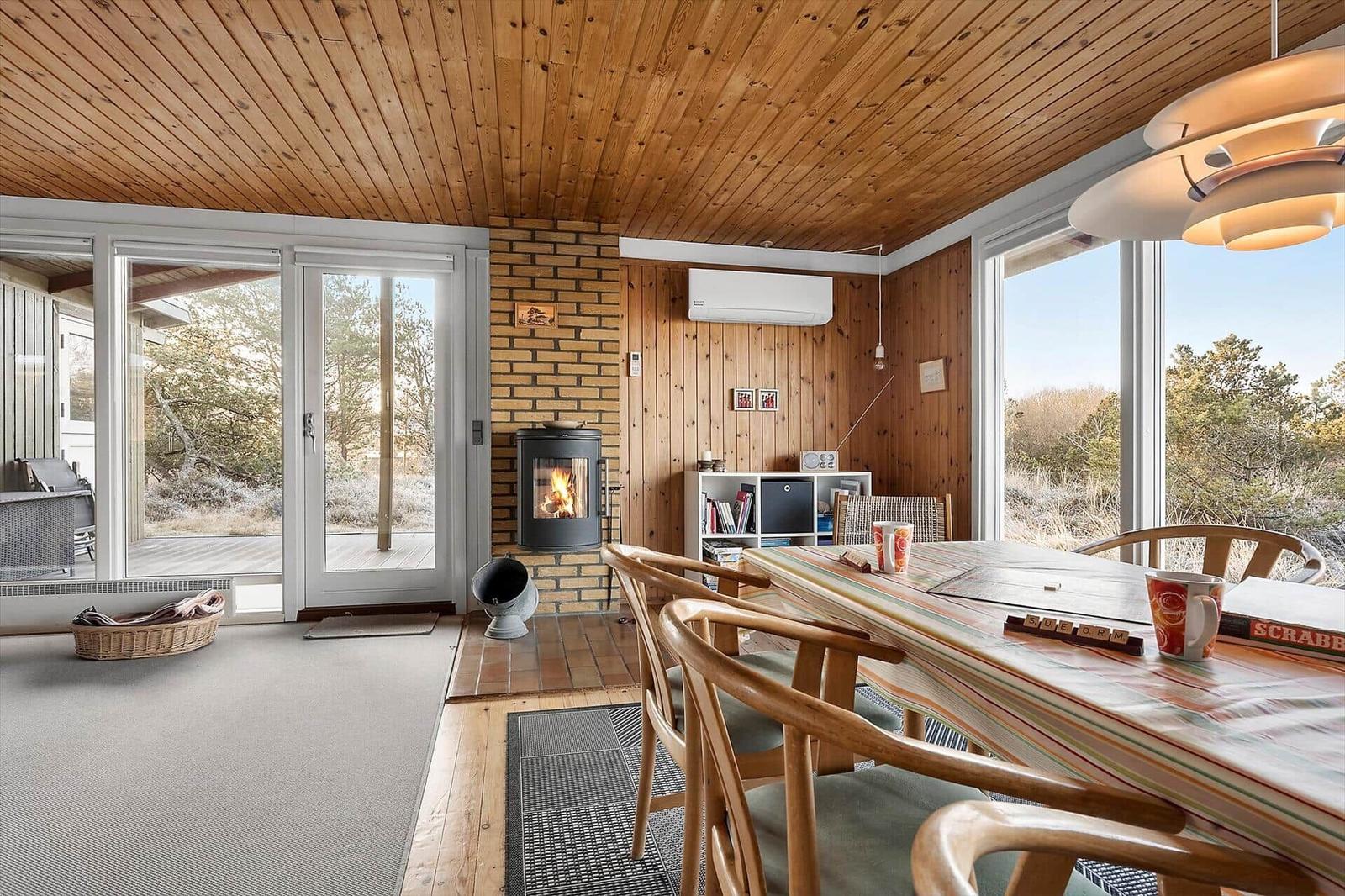 Esszimmer mit Holzdecke, Kamin und großem Fenster. Tisch mit Stühlen und Spielzeug.