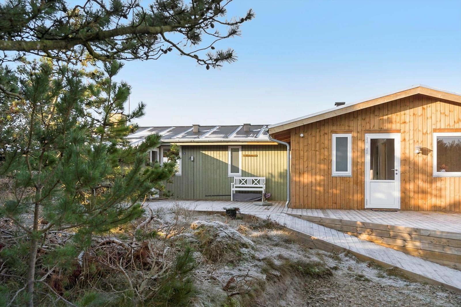 Holzhaus mit Terrasse und weißer Bank unter Bäumen