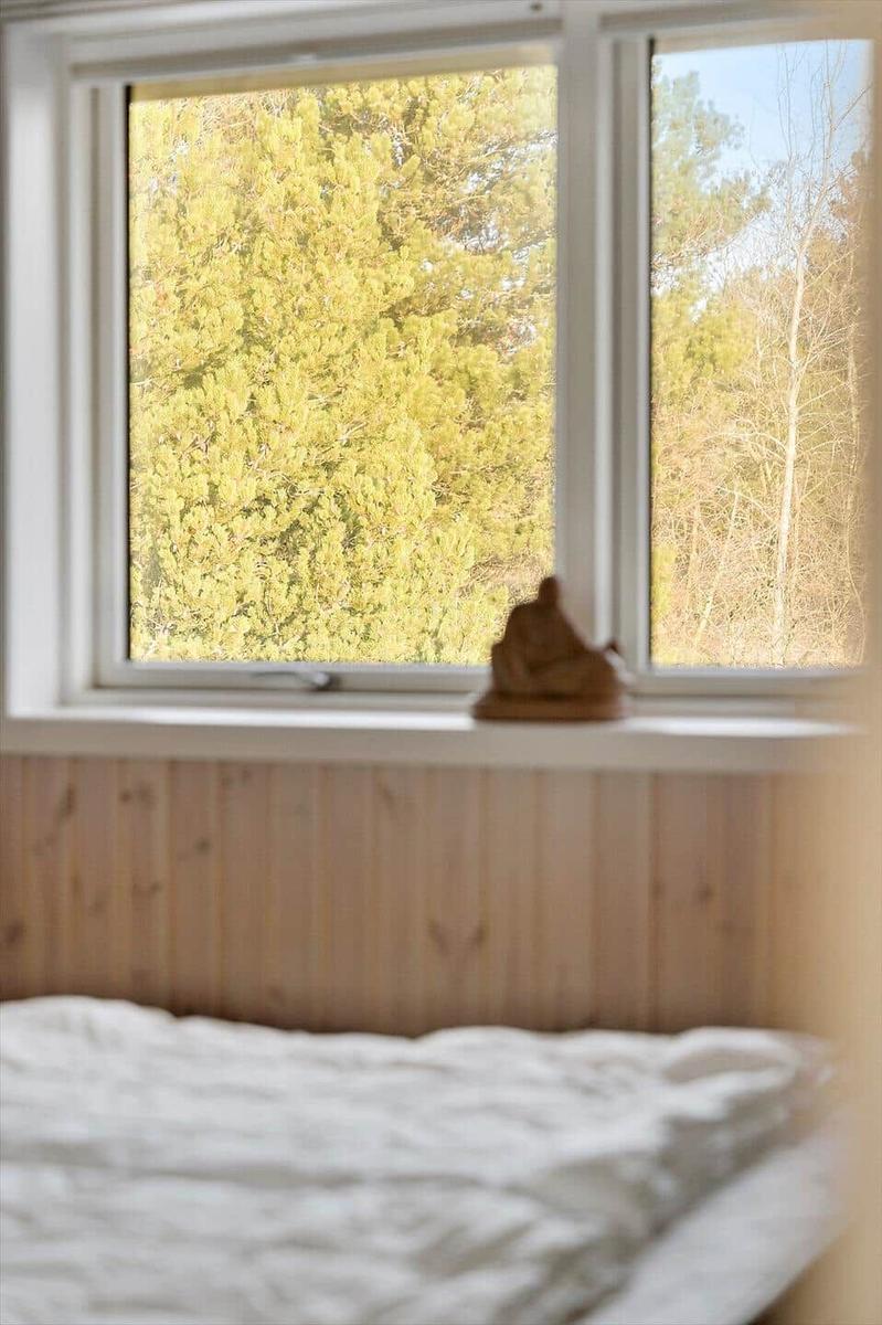 Ein Bett mit weißer Bettwäsche vor einem Fenster mit Blick auf Bäume.