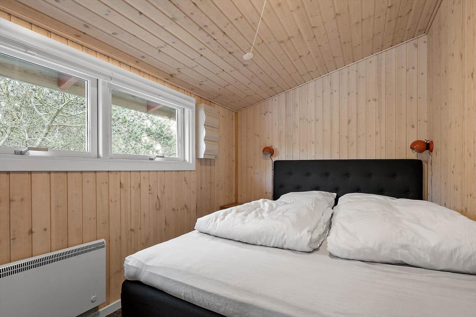 Schlafzimmer mit Holzwand, Bett, Fenster und Wandleuchten.