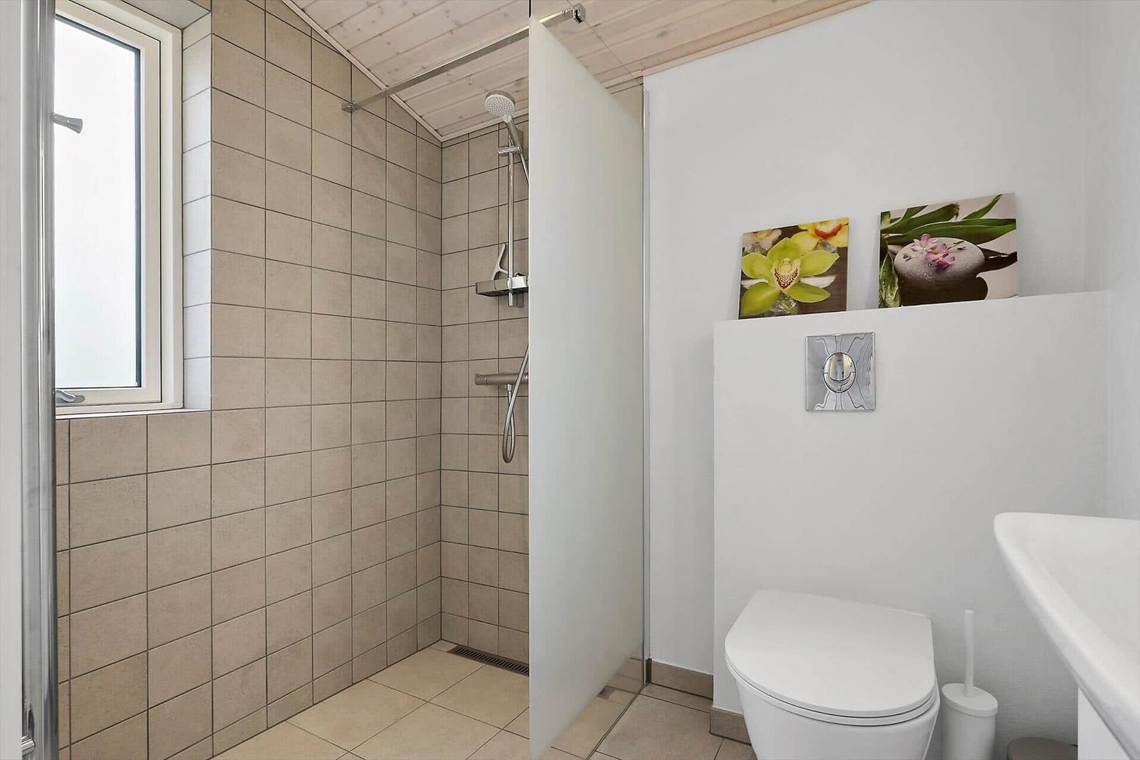Bad mit Dusche, Toilette und Waschbecken. Fenster, Wandbild und Holzdecke.