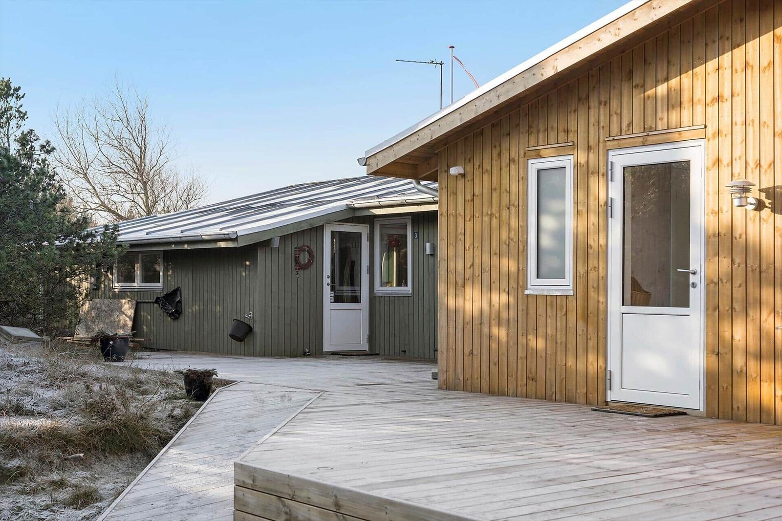 Holzverkleidetes Haus mit weißen Türen und Terrasse. Schnee bedeckt den Boden.