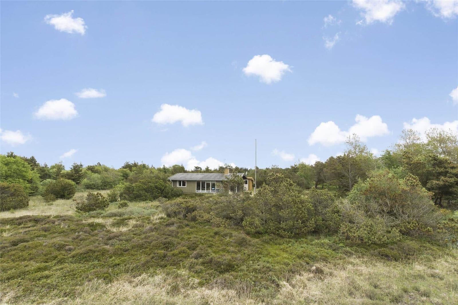 Ein Haus inmitten von Grünflächen und Bäumen unter einem blauen Himmel mit weißen Wolken.