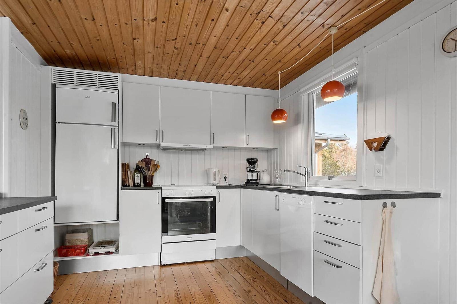 Küche mit weißen Schränken, Holzdecke und Fenster mit Blick nach draußen.
