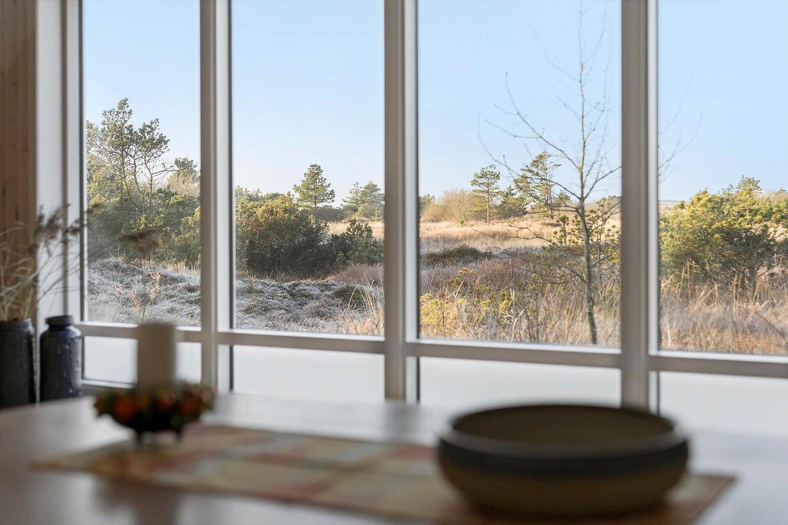 Durch große Fenster blickt man auf eine natürliche Landschaft mit Bäumen und Sträuchern.