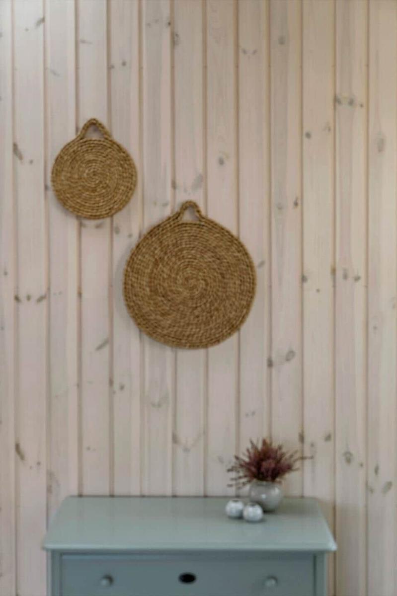Zwei runde, geflochtene Hängekörbe an einer Holzwand über einem Schrank mit Pflanze.