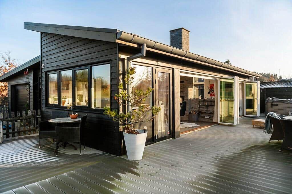 Moderne Holzhütte mit Terrasse, Glastüren und Sitzgelegenheiten im Freien.