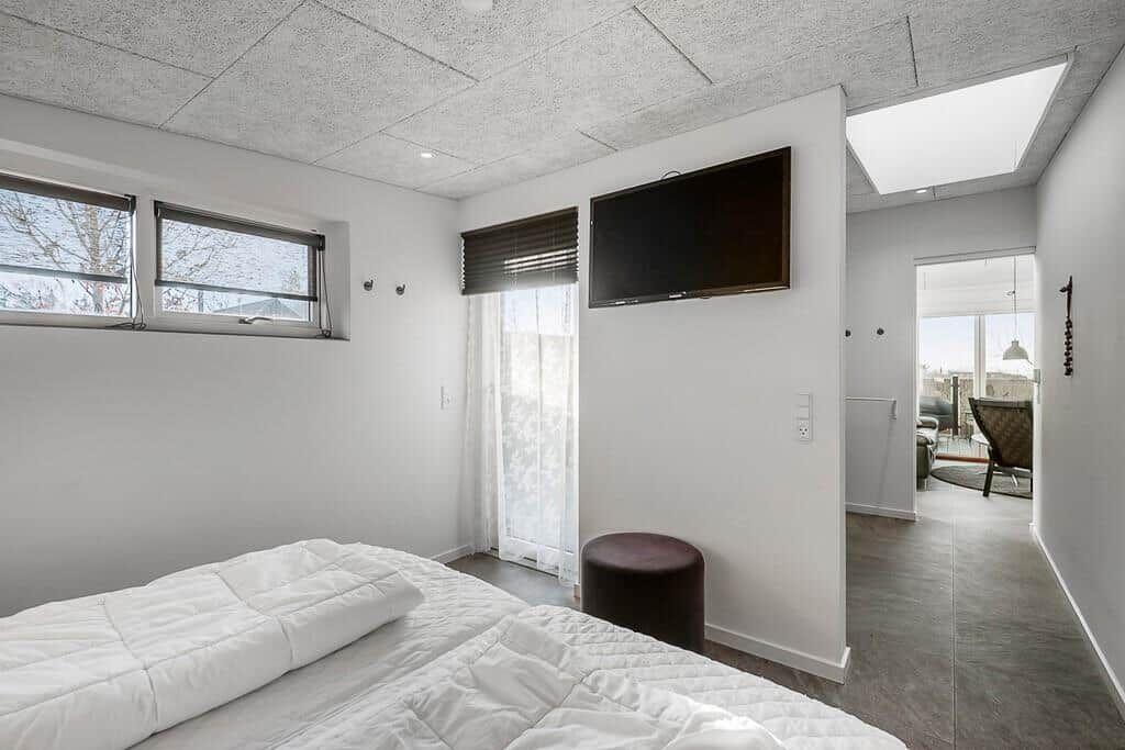 Schlafzimmer mit Bett, TV und Fenstern. Durchgang zur Wohnfläche.