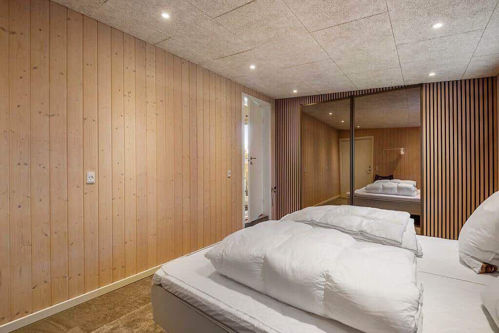 Schlafzimmer mit Holzwand und Spiegeltür. Bett mit weißen Kissen.