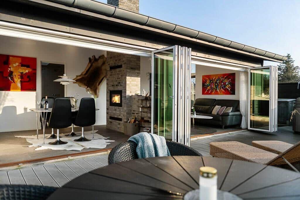 Terrasse mit Sitzgelegenheiten, die zum Innenraum mit Kamin und Essbereich führt.