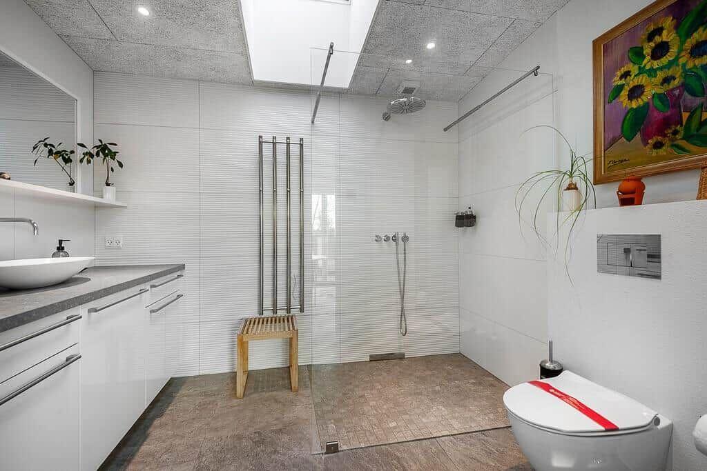 Badezimmer mit Dusche, Waschbecken und Toilette. Glaswand, Pflanzen und Wandbild.