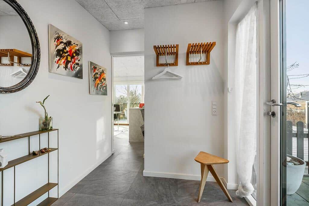 Eingangsbereich mit Wandbildern, Spiegel und Holzstuhl. Tür führt auf Balkon.
