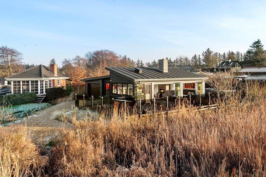 Moderne Villa mit großem Glasbereich und Terrasse, umgeben von Gras und Bäumen.