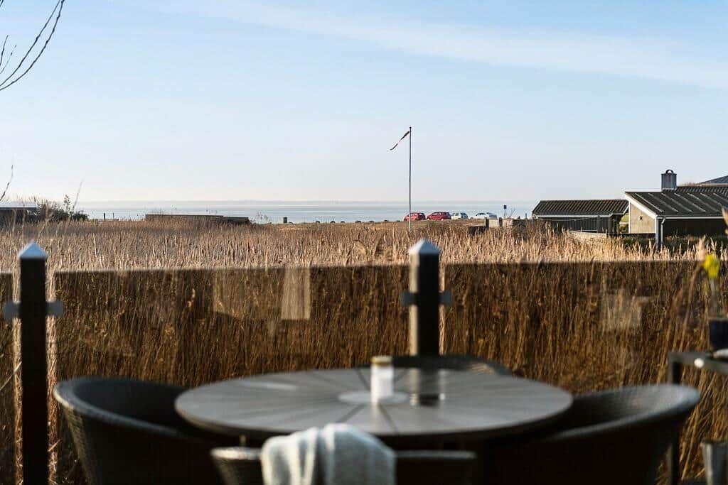 Terrasse mit Tisch und Stühlen, Blick auf Feld und Meer.