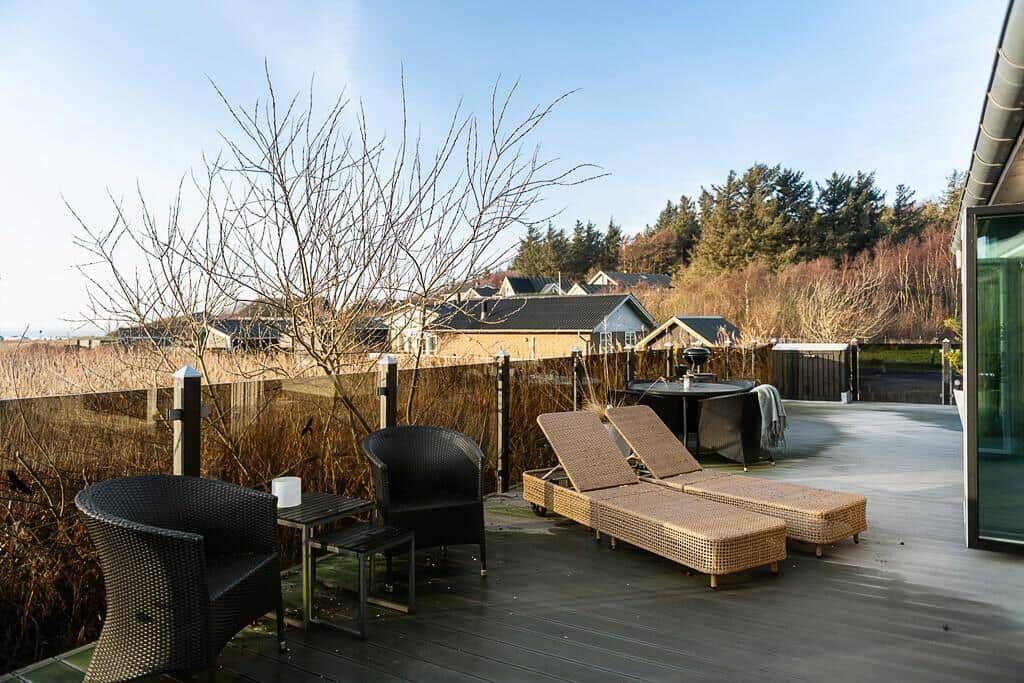 Terrasse mit Liegen, Sitzgelegenheiten und Blick auf Wohngebiet und Wald.
