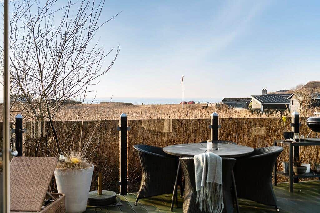 Terrasse mit Tisch, Stühlen und Blick auf Feld und Meer.